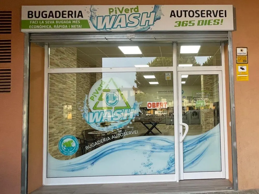 Fachada de la lavandería en Palafrugell: escaparate con el rótulo «Bugaderia autoservei, 365 dies» y la sala con las lavadoras al fondo